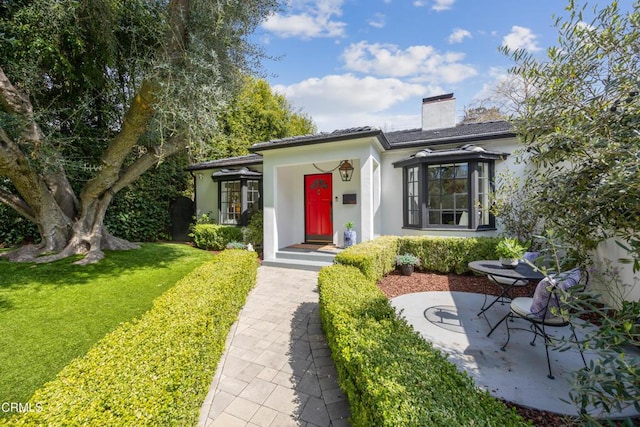 view of front of property featuring a patio area, stucco siding, a chimney, and a front yard