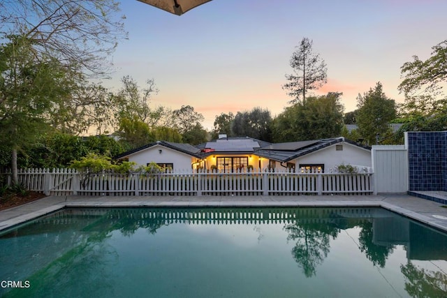 pool at dusk with a fenced in pool and fence