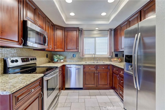 kitchen featuring a tray ceiling, light stone counters, decorative backsplash, appliances with stainless steel finishes, and a sink