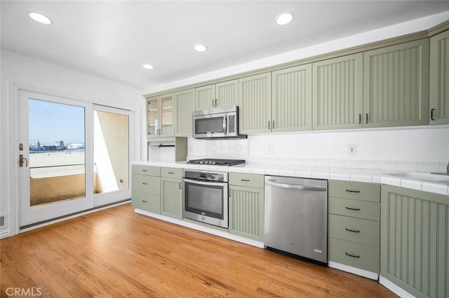 kitchen with recessed lighting, green cabinets, stainless steel appliances, and tile countertops