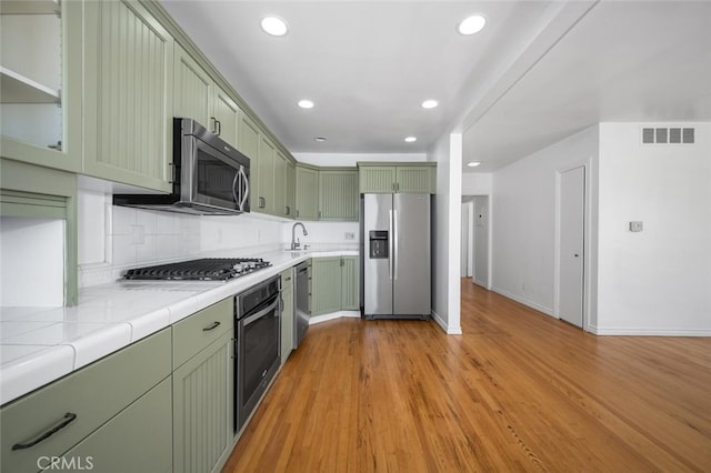 kitchen with tile counters, stainless steel appliances, baseboards, visible vents, and green cabinets