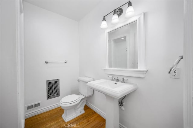 half bathroom with visible vents, baseboards, wood finished floors, and toilet