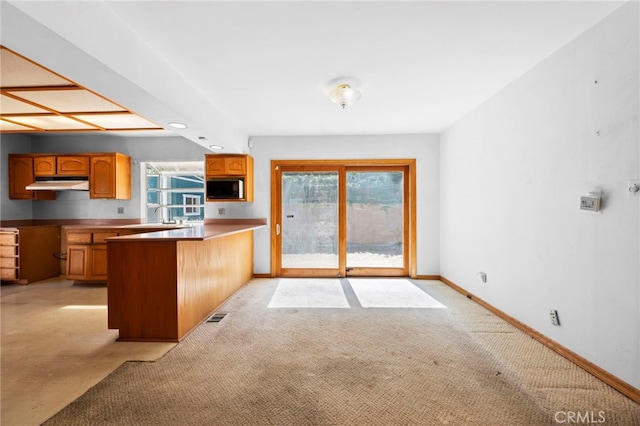 kitchen with baseboards, visible vents, a peninsula, built in microwave, and under cabinet range hood