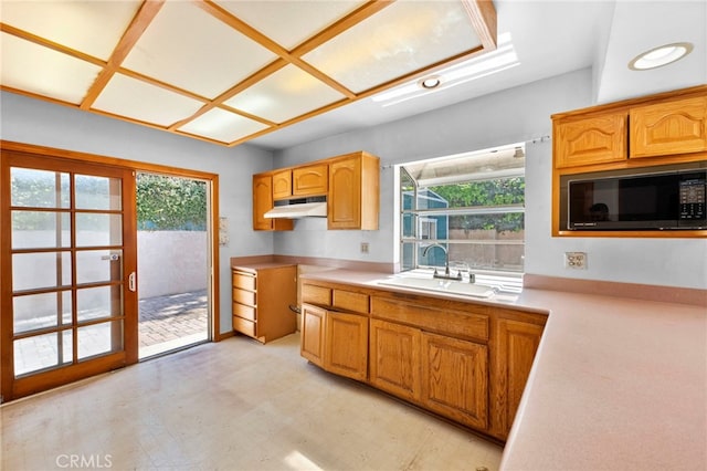 kitchen featuring light floors, a sink, light countertops, under cabinet range hood, and black microwave