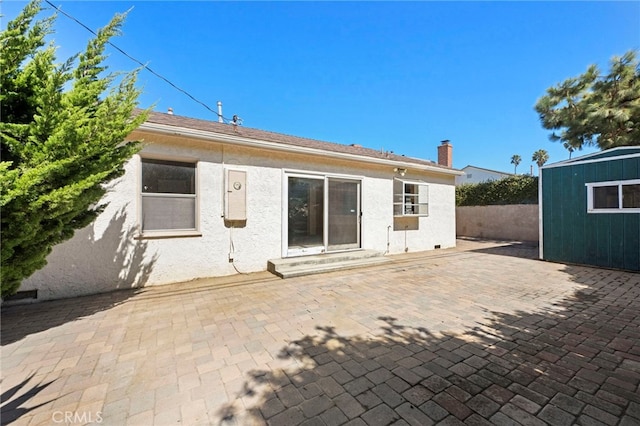 rear view of house with stucco siding, entry steps, a patio, an outdoor structure, and a chimney