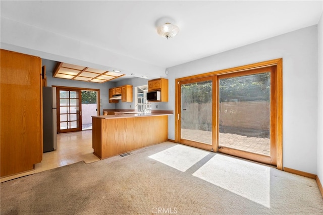 kitchen with visible vents, under cabinet range hood, freestanding refrigerator, a peninsula, and white microwave