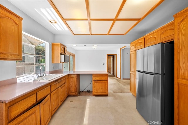 kitchen featuring light countertops, a peninsula, freestanding refrigerator, brown cabinetry, and a sink