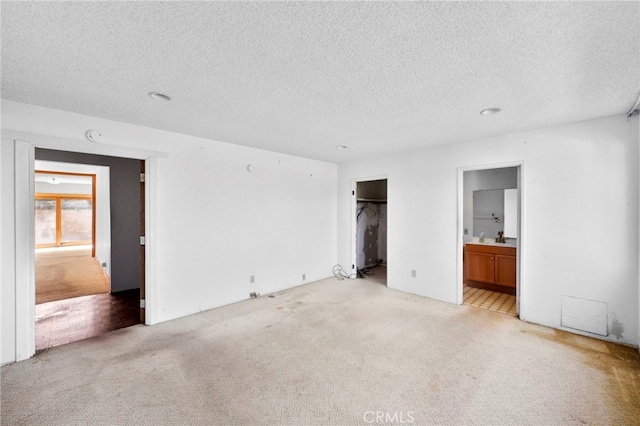 unfurnished bedroom with ensuite bath, a sink, a closet, a textured ceiling, and light carpet