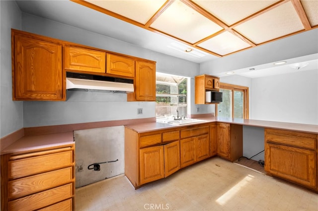 kitchen with brown cabinets, under cabinet range hood, a sink, light countertops, and light floors