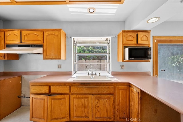 kitchen featuring under cabinet range hood, light countertops, black microwave, and a sink