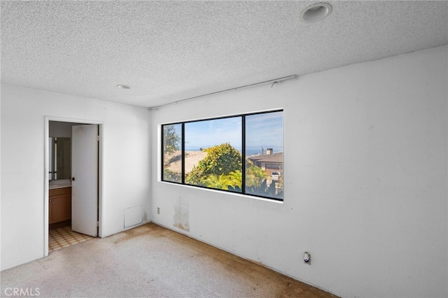 unfurnished bedroom with ensuite bath, carpet flooring, and a textured ceiling