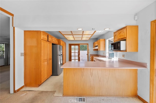 kitchen with visible vents, a peninsula, freestanding refrigerator, a sink, and black microwave