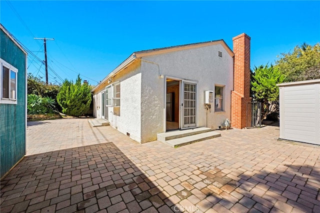 back of house with stucco siding, entry steps, a chimney, and a patio