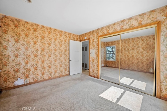 unfurnished bedroom with a closet, baseboards, wallpapered walls, and carpet