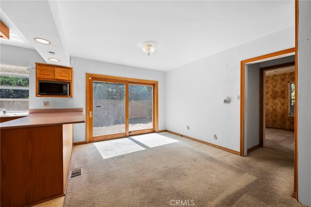 kitchen with brown cabinetry, baseboards, visible vents, black microwave, and light carpet