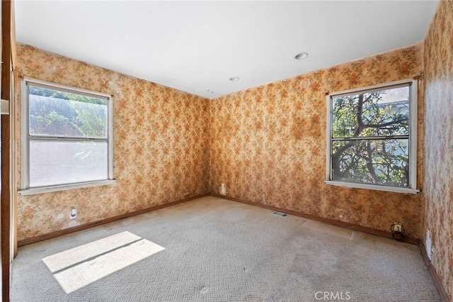 spare room featuring visible vents, baseboards, carpet, and wallpapered walls