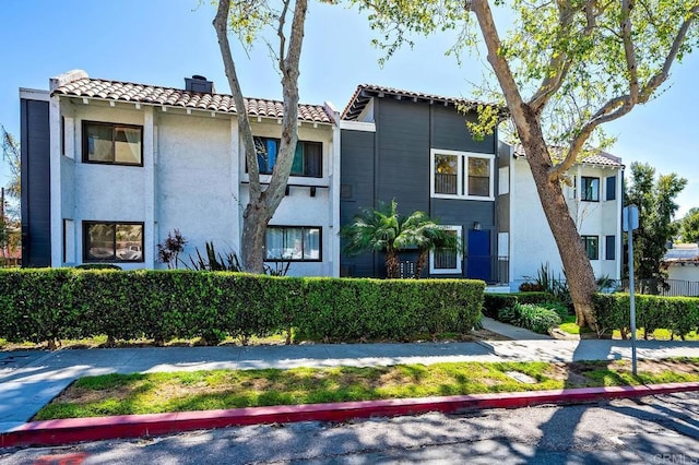 mediterranean / spanish-style house with stucco siding, a chimney, and a tiled roof