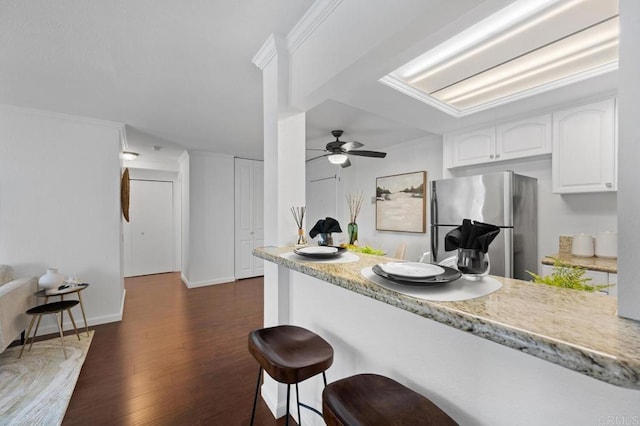 kitchen with dark wood-type flooring, freestanding refrigerator, a breakfast bar area, white cabinets, and light countertops