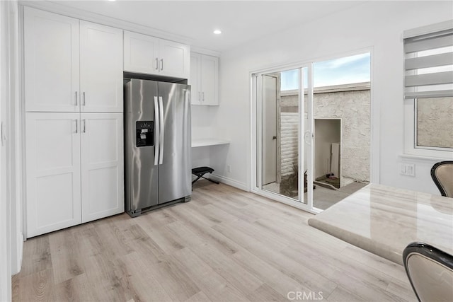 kitchen featuring light wood-type flooring, stainless steel refrigerator with ice dispenser, light stone counters, white cabinetry, and recessed lighting