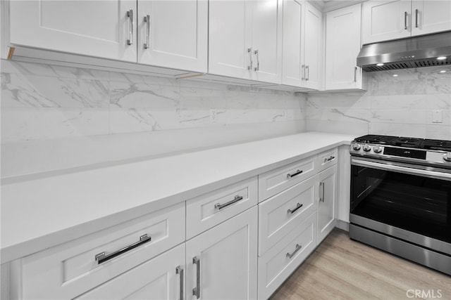 kitchen featuring under cabinet range hood, light countertops, decorative backsplash, light wood-style flooring, and stainless steel gas range