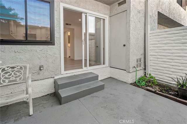 doorway to property featuring stucco siding, visible vents, and a patio area