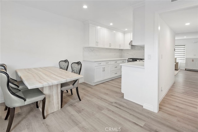 kitchen with tasteful backsplash, white cabinets, light countertops, and light wood-style floors