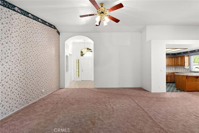 unfurnished living room with arched walkways, light colored carpet, wallpapered walls, and ceiling fan