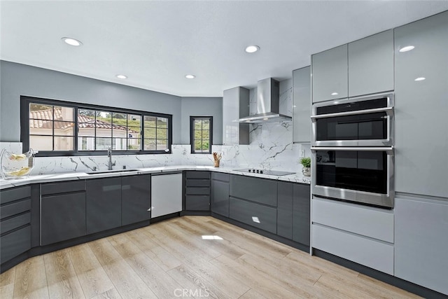 kitchen with a sink, gray cabinets, appliances with stainless steel finishes, and wall chimney range hood