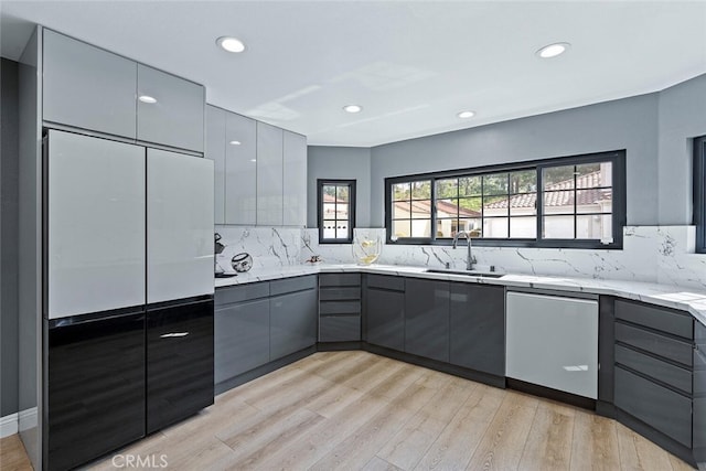 kitchen with a sink, gray cabinets, light wood finished floors, and backsplash