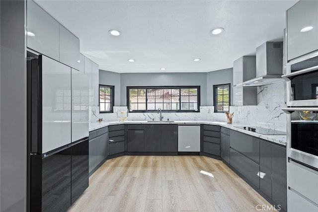 kitchen featuring wall chimney exhaust hood, gray cabinetry, a sink, stainless steel appliances, and light wood-style flooring