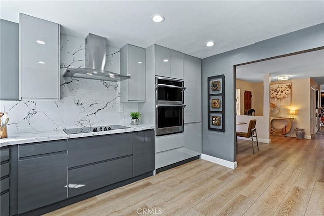 kitchen with decorative backsplash, light wood-style floors, black electric stovetop, gray cabinets, and wall chimney exhaust hood