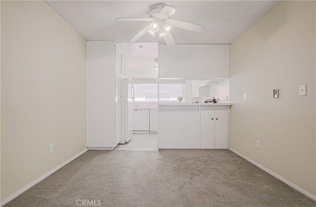 spare room featuring light carpet, baseboards, a ceiling fan, and a textured ceiling