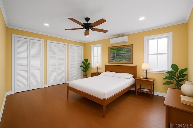 bedroom with a wall mounted air conditioner, crown molding, hardwood / wood-style flooring, and multiple closets
