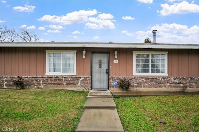 doorway to property with brick siding and a lawn