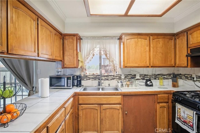 kitchen featuring a sink, stainless steel microwave, ornamental molding, and tile countertops