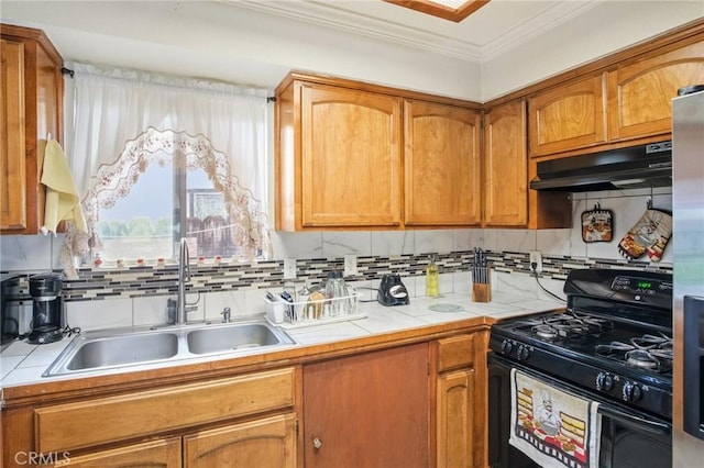 kitchen featuring gas stove, ornamental molding, a sink, tile counters, and under cabinet range hood