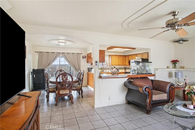 kitchen featuring brown cabinets, a ceiling fan, stainless steel fridge, crown molding, and light tile patterned floors