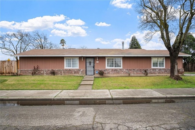 ranch-style home featuring brick siding, roof with shingles, a front yard, and fence