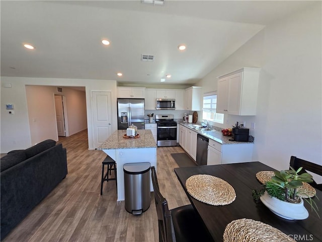 kitchen with a kitchen island, wood finished floors, white cabinetry, stainless steel appliances, and a breakfast bar area