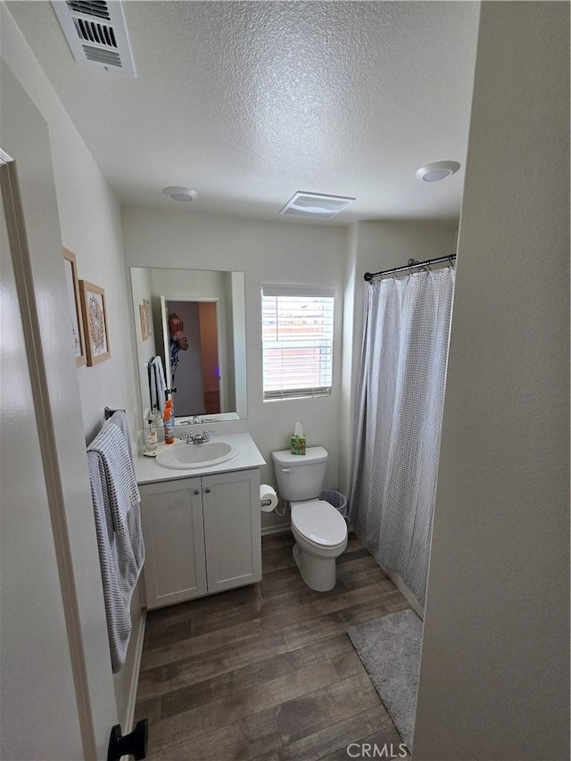 full bathroom with vanity, wood finished floors, visible vents, a textured ceiling, and toilet