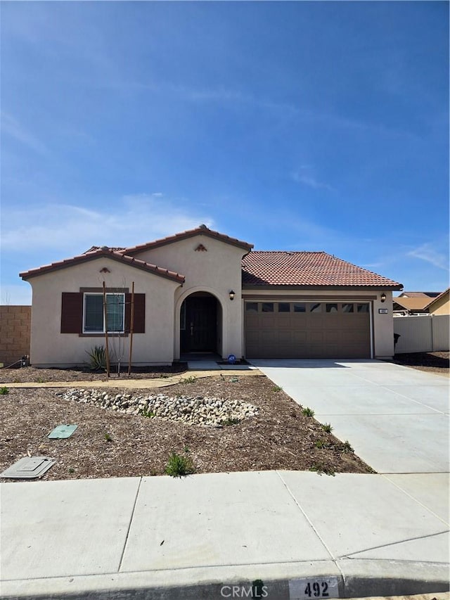 mediterranean / spanish-style home featuring stucco siding, a tiled roof, an attached garage, and driveway