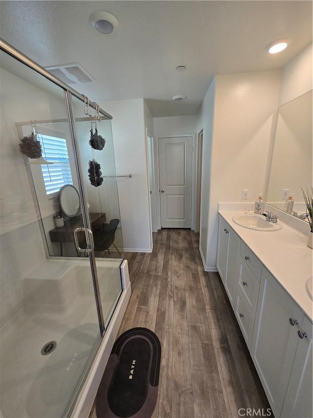 full bathroom with a stall shower, a sink, wood finished floors, double vanity, and baseboards