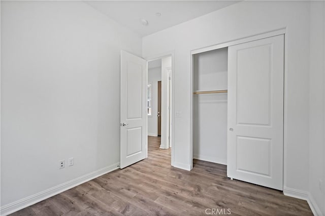unfurnished bedroom featuring baseboards, wood finished floors, and a closet