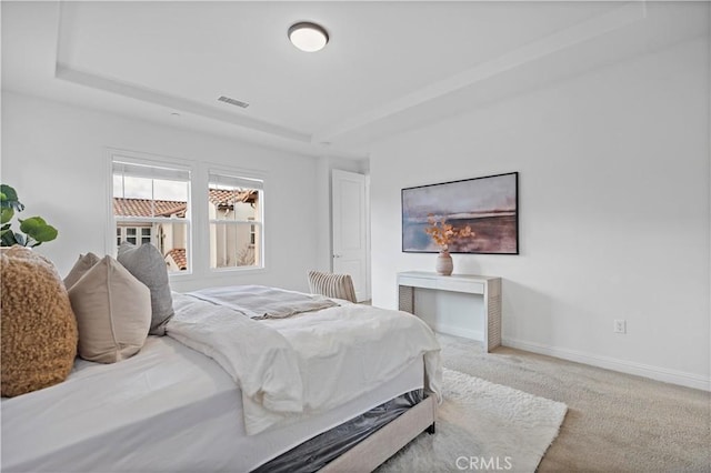 bedroom with carpet floors, a tray ceiling, baseboards, and visible vents