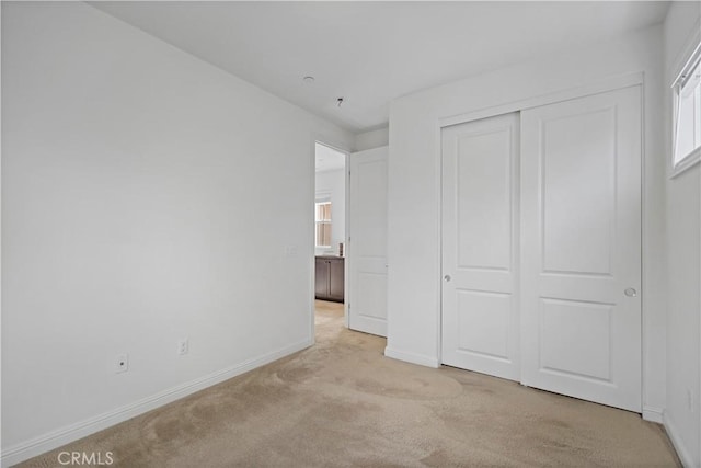unfurnished bedroom featuring baseboards, a closet, and light colored carpet
