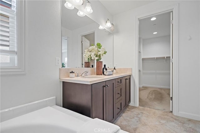 full bathroom with vanity, a walk in closet, and baseboards