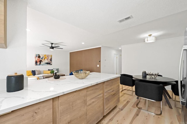 kitchen featuring visible vents, light wood-style flooring, a textured ceiling, light stone countertops, and ceiling fan