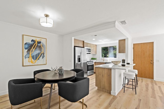 kitchen featuring a breakfast bar, light wood finished floors, visible vents, and appliances with stainless steel finishes