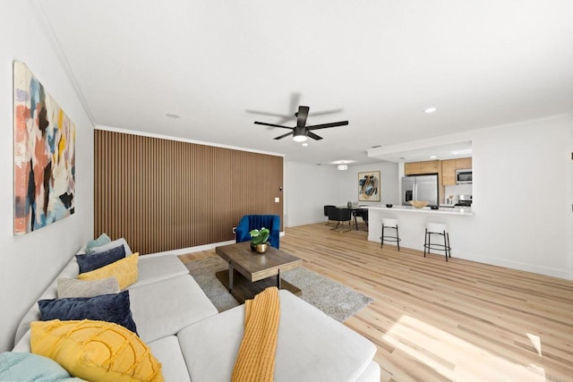 living room featuring baseboards, light wood-style floors, ceiling fan, and crown molding