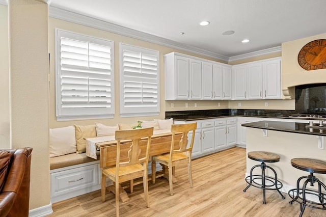 2185 Twain Ave, Carlsbad, CA 92008 - kitchen featuring white cabinetry, dark countertops, ornamental molding, a breakfast bar, and light wood-type flooring